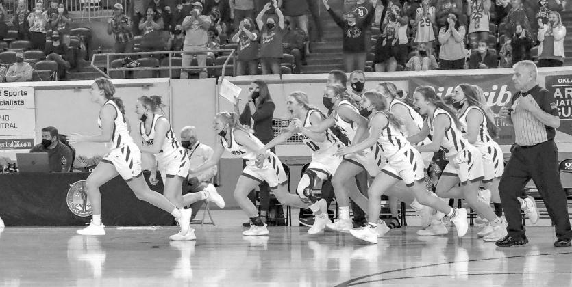 PILING IT ON — Lomega’s bench (above) rushes the court after the final buzzer to celebrate the team’s Class B state championship victory over Kiowa. Lomega finished 27-0 in winning its second straight state championship and 15th overall. [Photo by C Lomega runs to perfection
