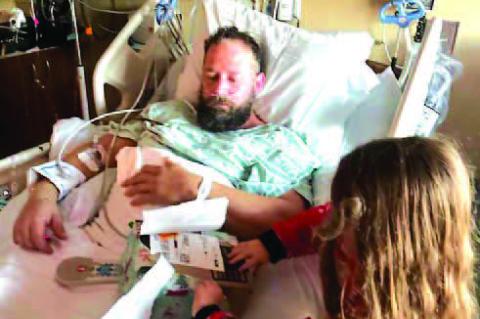 MATT SCOTT lays in a hospital bed after nearly 12 hours of surgery on Christmas Eve as his 6-year-old daughter Charlie opens gifts. [Photo provided]